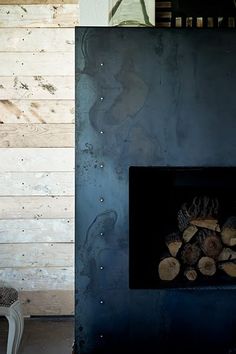 a fire place with logs in front of it and a chair next to the fireplace