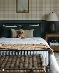 a teddy bear sitting on top of a bed in a room with plaid wallpaper