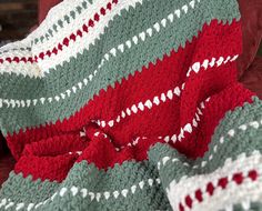 a crocheted blanket is draped over a couch with a red and green throw