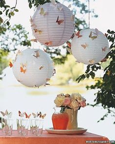 three paper lanterns hanging from a tree with butterflies on them, one is white and the other is pink