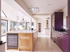 a large kitchen with purple cabinets and an island in the middle is shown, as well as a wine refrigerator