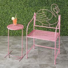 a pink metal chair next to a table with a drink on it and a green wall behind it