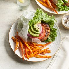 two plates with burgers and french fries on them, next to a glass of water