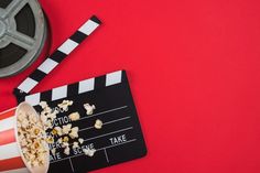 a movie clapper next to a bowl of popcorn on a red background with a film reel