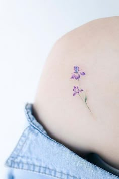 a small tattoo on the back of a woman's stomach with purple flowers growing out of it