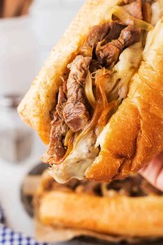 a close up of a person holding a sandwich in their hand with meat and onions on it