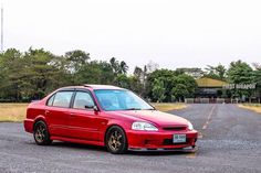 a red car parked on the side of a road next to a field and trees