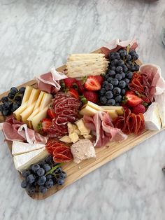 an assortment of cheeses, fruits and meats on a wooden platter sitting on a marble counter top