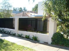 a white house with a black fence and some plants on the side walk in front of it