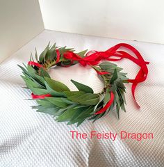 a wreath made out of leaves and red ribbon on top of a white sheet with the words the festy dragon