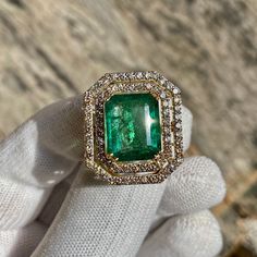 a close up of a person's hand holding an emerald and diamond ring