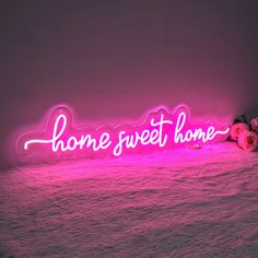 a pink neon sign that says home sweet home with flowers on the ground next to it