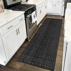 a kitchen with white cabinets and an area rug on the floor in front of the stove