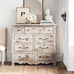 an old dresser with flowers on top and a mirror in the corner next to it