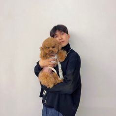 a young man holding a teddy bear in his arms while standing against a white wall