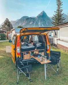 the back end of an orange van parked on top of a grass covered field next to a picnic table