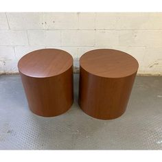 two wooden stools sitting next to each other on a cement floor in front of a white brick wall