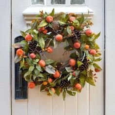 a wreath is hanging on the front door with pine cones and oranges around it