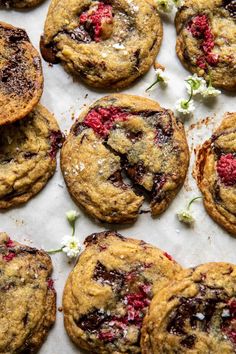 chocolate chip cookies with raspberries and white flowers on a sheet of parchment paper