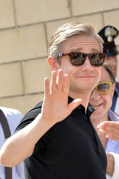 a man in sunglasses making the vulcan sign with his hand as he stands next to other people