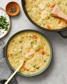 two bowls of chicken and dumpling soup on a white table with wooden spoons