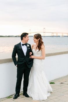 a bride and groom standing next to each other near the water in front of a bridge