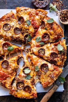 a pizza with pepperoni and olives on a cutting board next to some spices