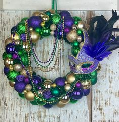 a mardi gras wreath is hanging on a white wooden door with beads and feathers