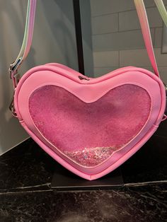 Bonjour!  The Lil' Heartbreaker is a heart shaped bag with amazing details at every curve!  It measures approximately 9" wide, 9" tall, and 3" deep.  It has a double zipper closure at the top of the heart and the strap connectors are on either side of the zipper.  It features a clear vinyl front with iridescent pink glitter inside that moves and jiggles as you walk.  So cute!  The pink vinyl outer is so soft and the silver hardware contrasts it nicely.  The 1" strap connectors are reinforced with heart shaped rivets, the zipper pulls say "Bee mine", and there is a tag on the back that says, "Don't go break-in' my heart".  The strap is removable and adjustable in a rainbow colored seatbelt webbing.  Open it up to reveal hearts and polka dots water resistant canvas lining  and a white mesh s Clear Stadium Bag, Heart Shaped Bag, Stadium Bag, Pink Vinyl, Bee Mine, Clear Vinyl, White Mesh, Zipper Pulls, Pink Glitter