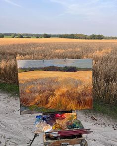 an artist's easel with his painting on it in front of a cornfield