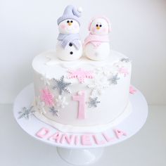 two snowmen on top of a white cake with pink frosting and the number one