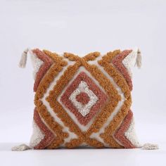 an orange and white pillow with tassels on the sides, sitting on a white surface