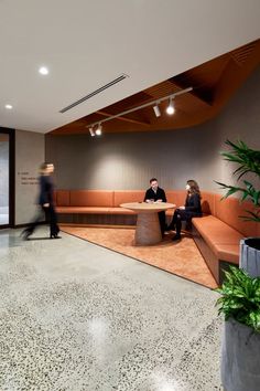 two people are sitting at a table in an office lobby with large planters on the floor