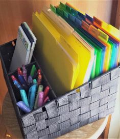 a basket filled with lots of different colored pens and folders on top of a table