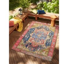 a colorful rug on a wooden deck with benches and potted plants in the background