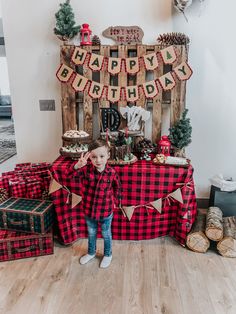 a little boy standing in front of a birthday cake table with plaid cloth on it