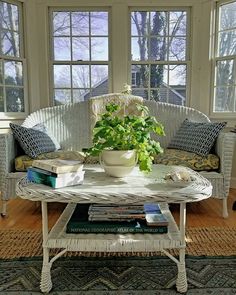 a white wicker couch sitting next to a table with a potted plant on it