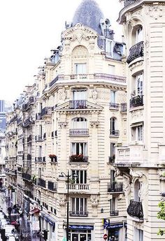 a city street filled with lots of tall buildings next to traffic and people walking on the sidewalk