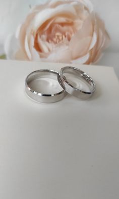 two wedding rings sitting on top of a white surface next to a pink rose and flower