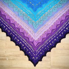 a blue and purple crocheted shawl sitting on top of a wooden floor