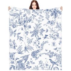 a woman holding up a large blue and white floral print blanket with birds on it