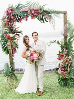 a bride and groom standing under an arch decorated with tropical flowers at their wedding ceremony