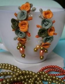 two pairs of orange and green flower earrings on a table next to pearls, beads and a cup