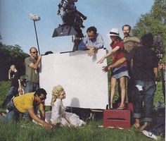 a group of people standing around a giant white board in the grass with a camera on it