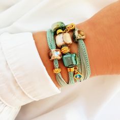 Women's bracelet in turquoise, beige and gold tones. This bohemian-style bracelet with a chic touch is made with a turquoise, aquamarine, light blue cotton ribbon that wraps around your wrist three times and is tied at the back. It is decorated with several charms of different styles, Greek porcelain beads, golden charms and two hanging light points. This bracelet has a bohemian touch but is very elegant and distinguished. Give your look a modern and youthful point with chic airs. -------------- Elegant Turquoise Bracelets For Beach, Turquoise Bracelet Jewelry, Turquoise Bracelet Fashion Accessory, Turquoise Fashion Bracelet, Elegant Turquoise Adjustable Charm Bracelet, Bohemian Gold Crystal Bracelet Hand Wrapped, Gold Bohemian Friendship Bracelets, Bohemian Green Crystal Bracelet For Beach, Bohemian Gold Hand Wrapped Crystal Bracelet