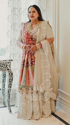 a woman standing in front of a window wearing a white and red outfit with gold jewelry