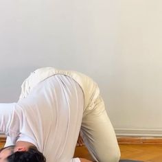 a man in white shirt and black pants doing a yoga pose with his hands on the ground