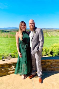 a man and woman standing next to each other in front of a green field with trees