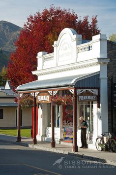 an old fashioned pharmacy store on the corner of a street with autumn trees in the background