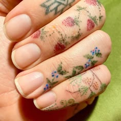 a woman's hand with tattoos on it and flowers painted on her fingers,